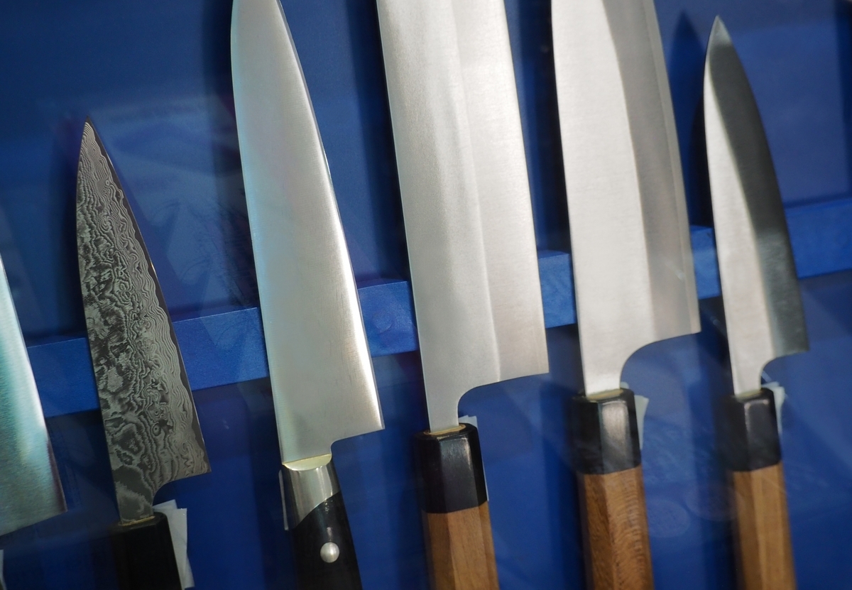 青い布の上に並べられた牛刀や三徳など各種包丁の刃先と木柄