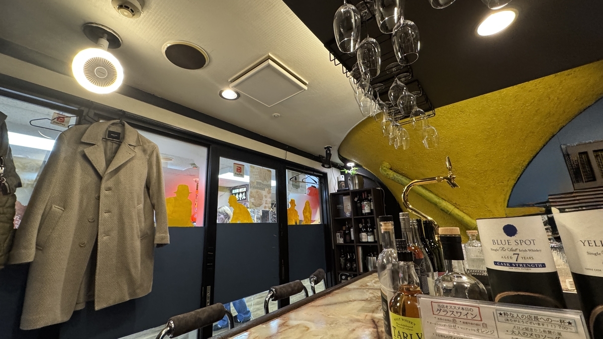 大理石風のカウンターとワイングラスが吊られた店内 青と黄の壁にボトル棚とタップが並ぶ内観