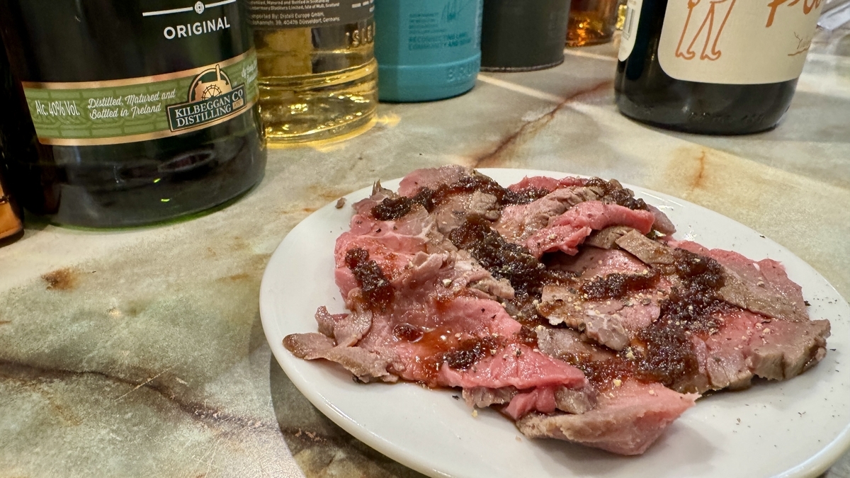 ローストビーフを薄くスライスして盛り付けた一皿 粗挽き胡椒とソースがかかった肉料理