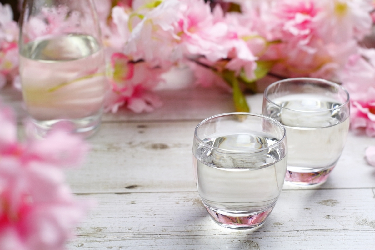 桜の花の前に置かれた日本酒の瓶と二つのグラスに注がれた透明な酒