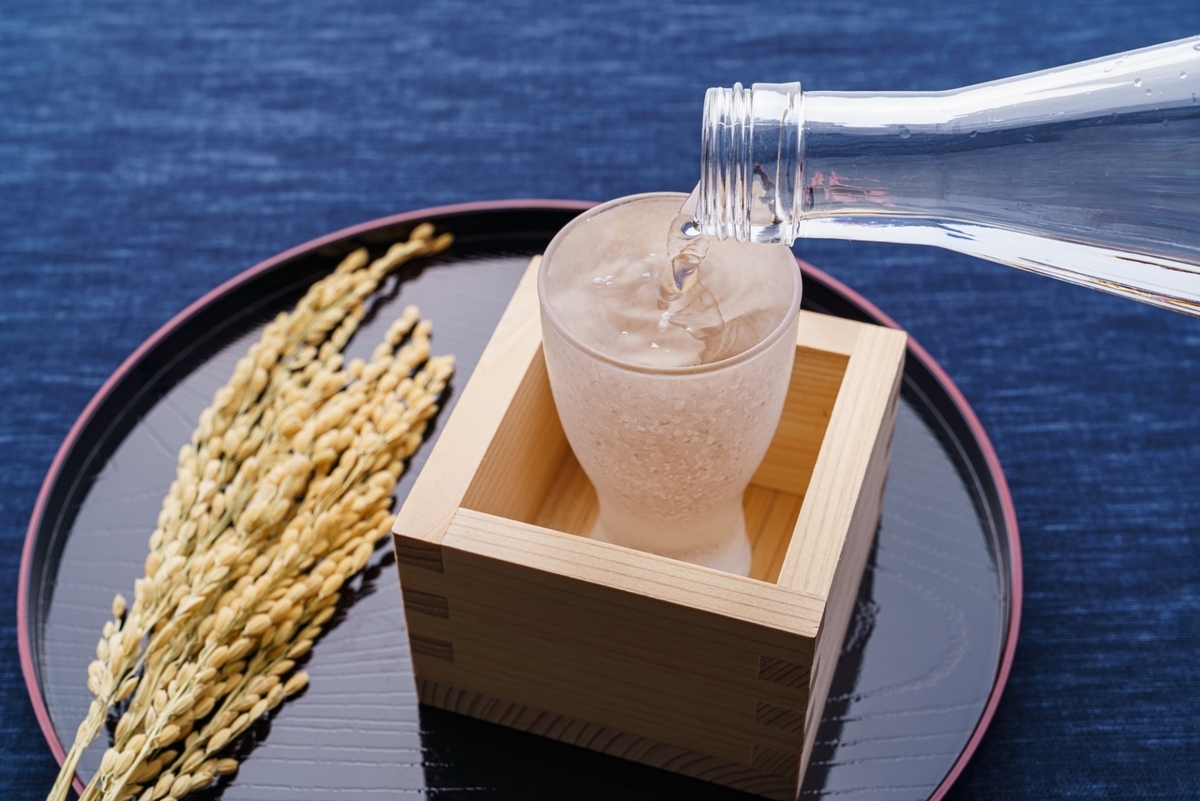 明るい木目の棚に日本酒ボトルが並ぶ白基調の試飲スペース中央のテーブルと盆栽