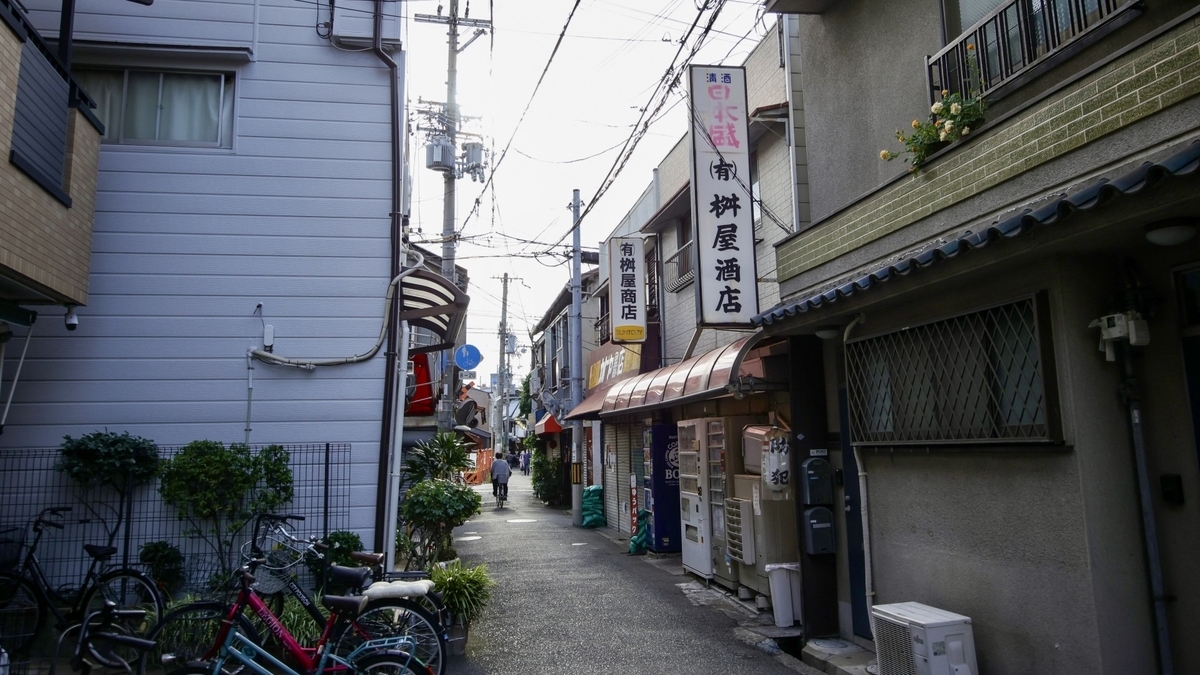 住宅街の細い路地に立つ老舗酒屋の看板と自転車が見える街並み