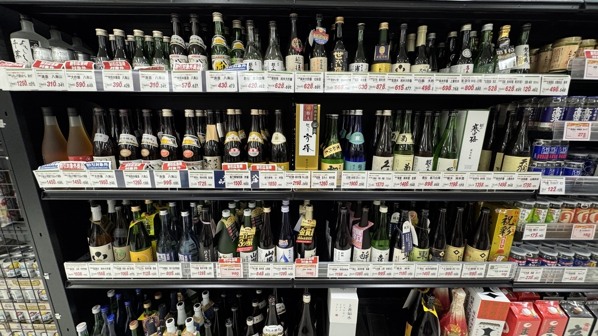 スーパーの冷蔵棚いっぱいに並ぶ日本酒ボトルと値札が続く売場