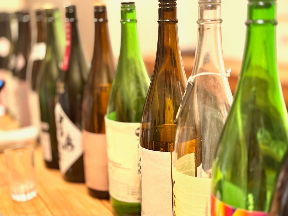 角打ちカウンターに一列に並ぶ日本酒ボトルと空のグラス
