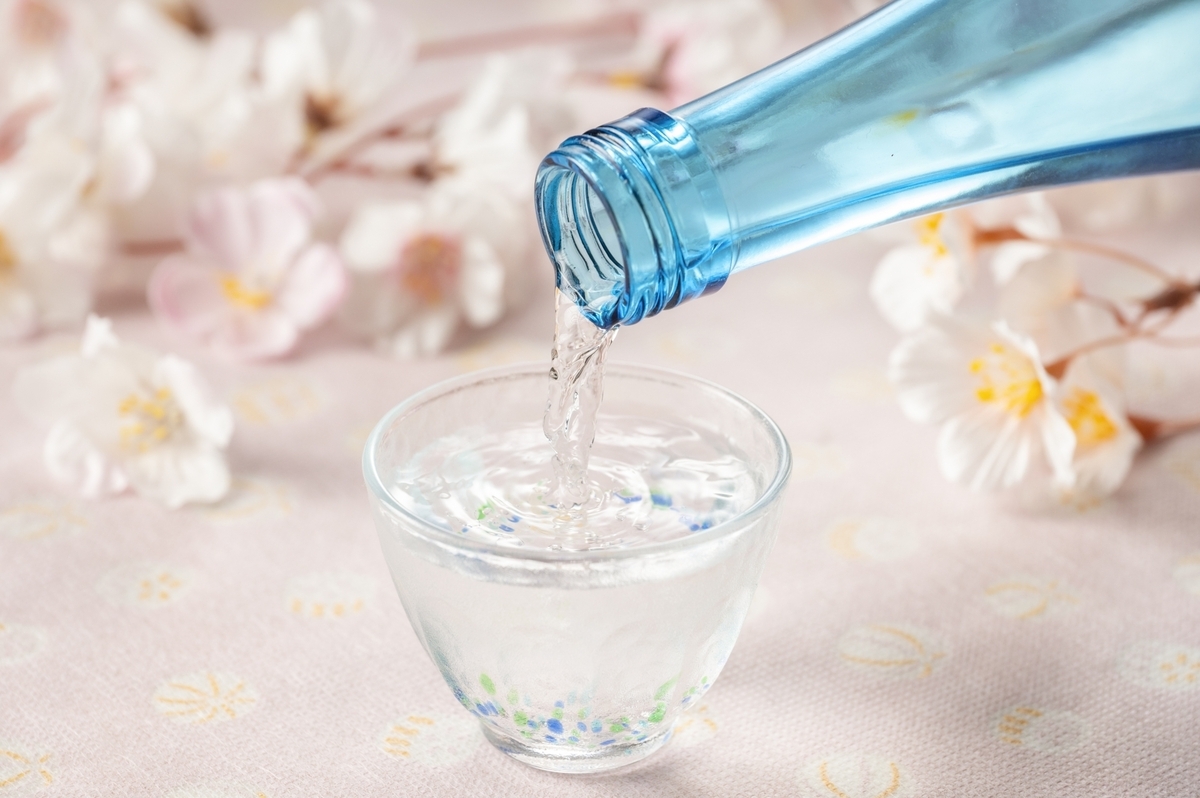 桜の花を背景に青い瓶からガラス盃へ日本酒を注ぐ春らしい構図