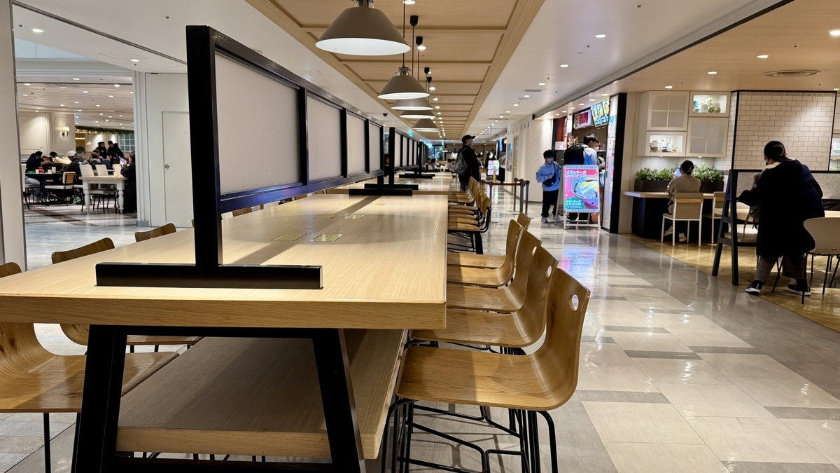 モザイク柄の長テーブル席と装飾照明が見えるミアキッチン前の共有ダイニング空間