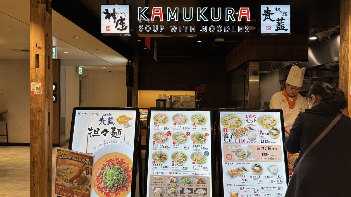 神座と青藍の連名サインの下に麺メニュー看板が並ぶ注文カウンター