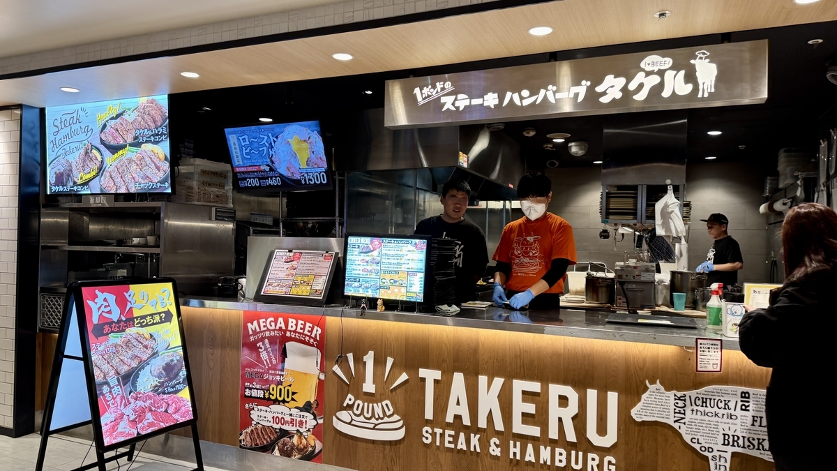 ステーキ写真の看板と調理スタッフが見えるタケルのオープンキッチン