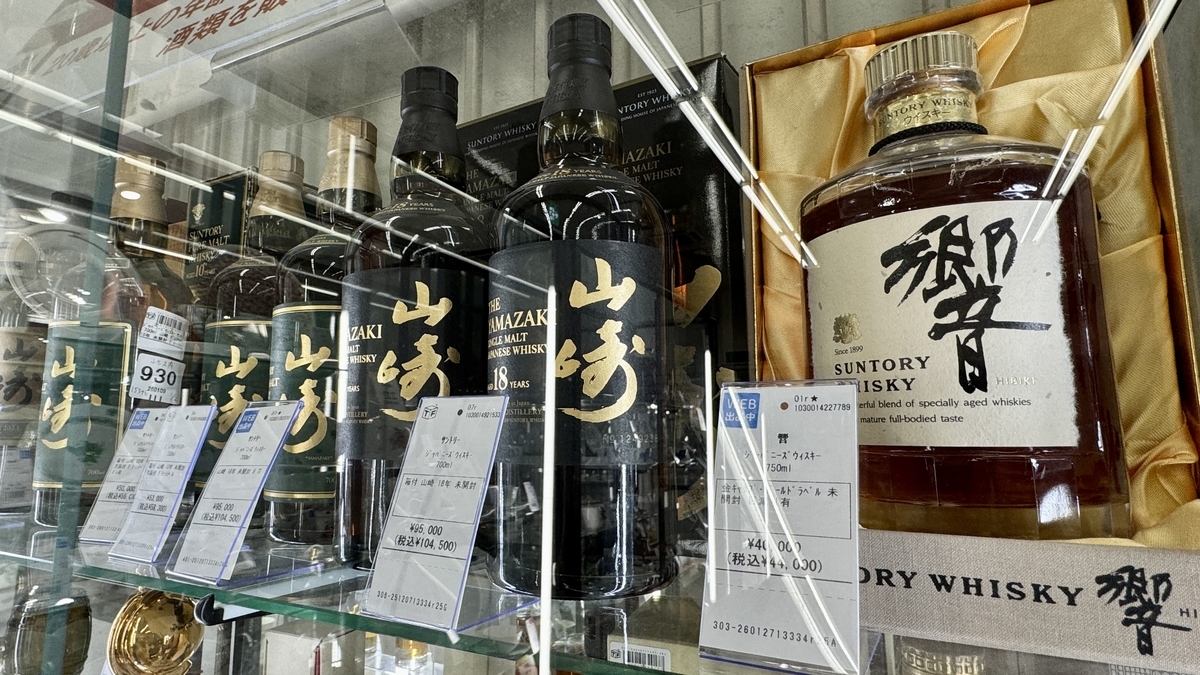 酒販店のガラスケースに山崎や響のボトルと価格札が並ぶ販売棚