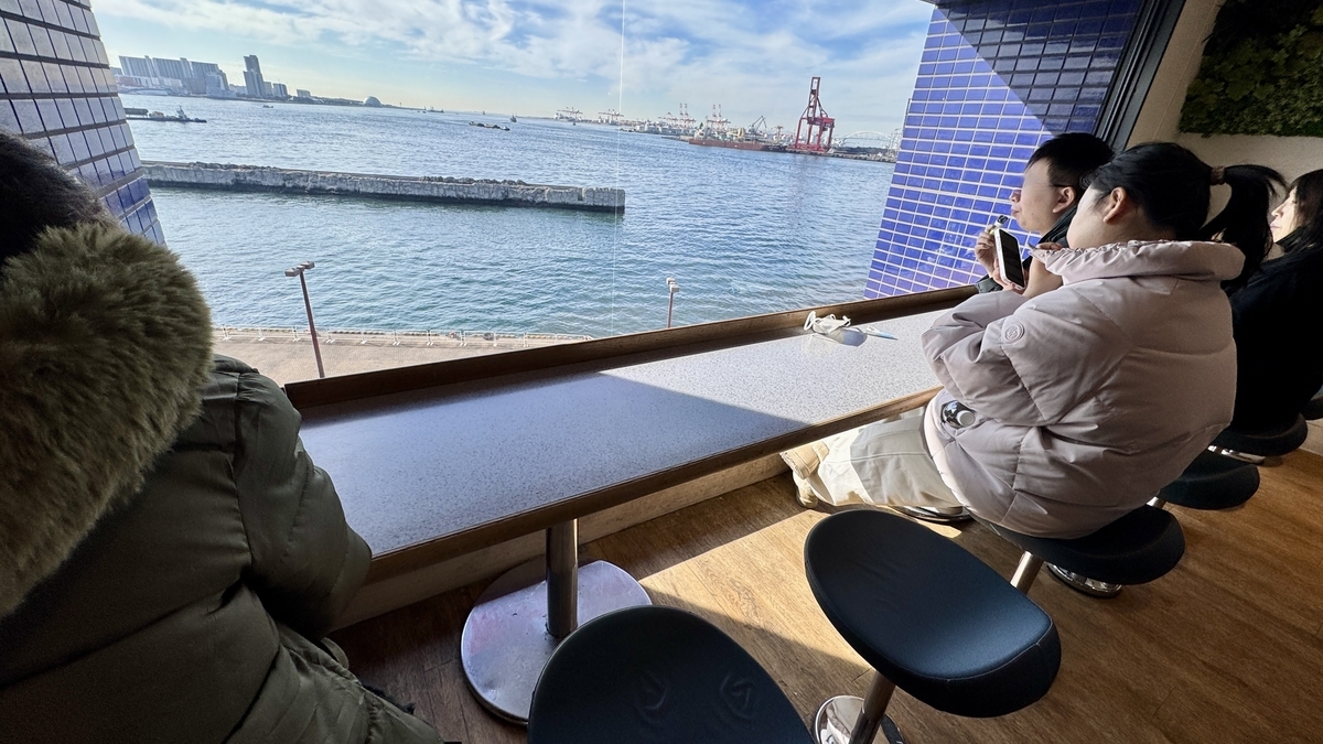 大阪湾を見下ろす窓際カウンター席で来店者が休憩する様子