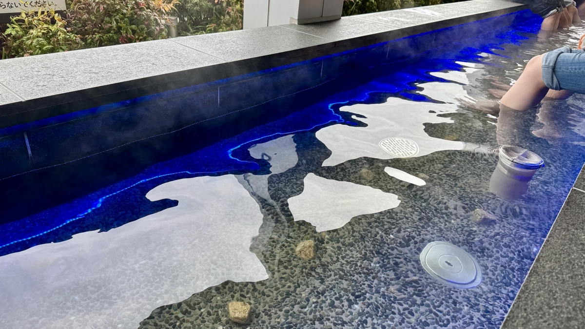 青い縁取りが映る足湯の湯面と足裏用の石