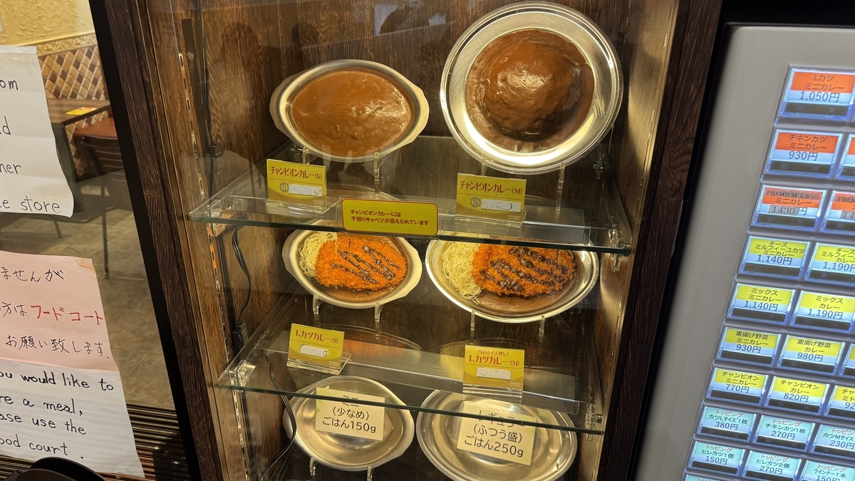 券売機横のショーケースに並ぶチャンピオンカレーとLカツカレーの食品サンプル