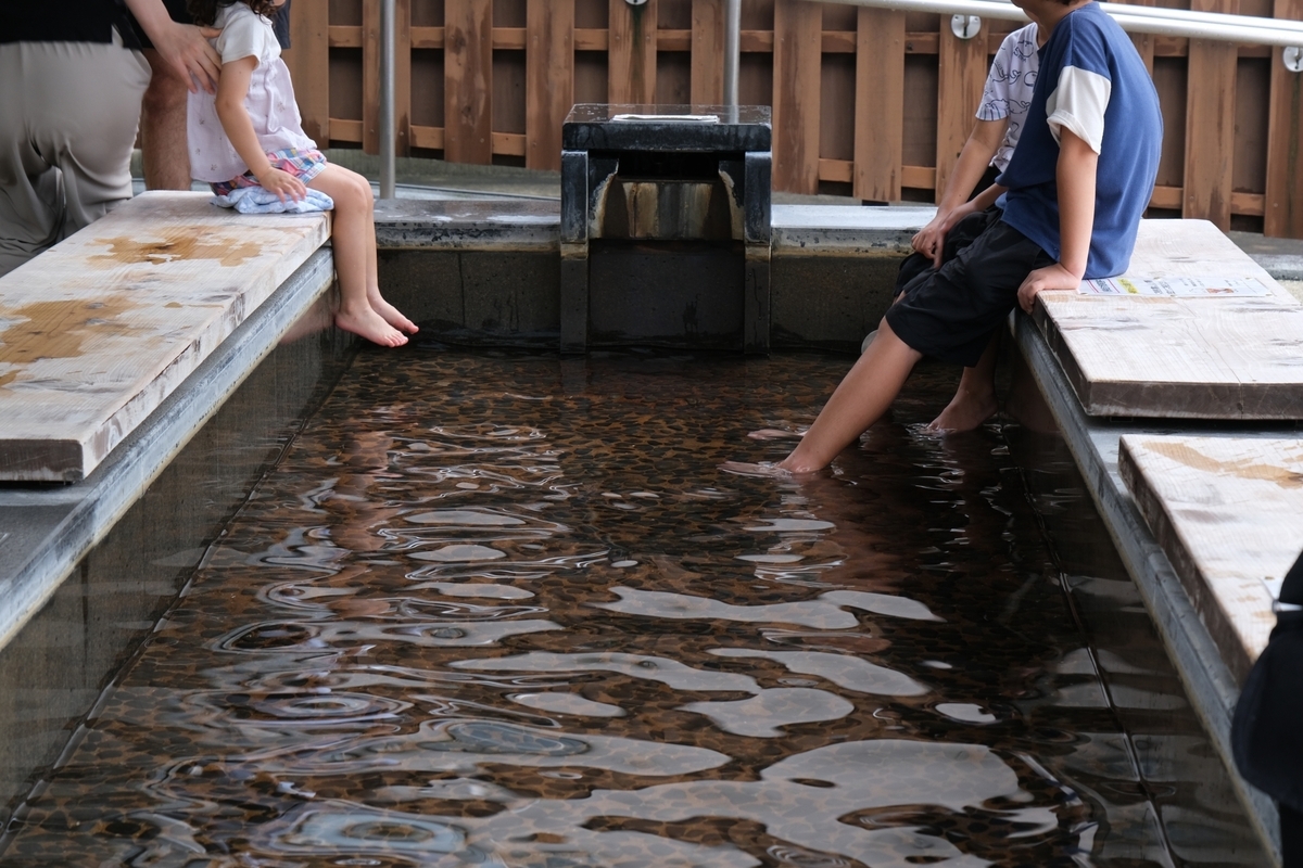 木の囲いがある足湯で湯に足を浸す人々