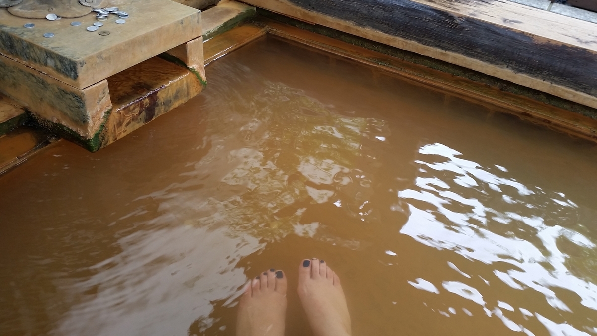 茶褐色の温泉に足を浸す木枠の足湯