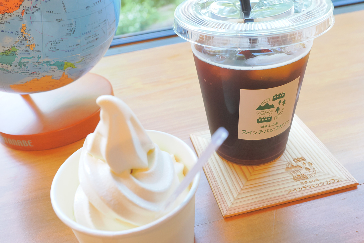 スイッチバックカフェの窓際で、アイスコーヒーとソフトクリームが置かれたテーブル