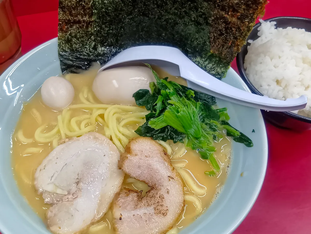 横浜家系 ラーメン壱七家の家系ラーメンとライス。ラーメンにはチャーシュー、ほうれん草、海苔、うずらの卵が乗っている。