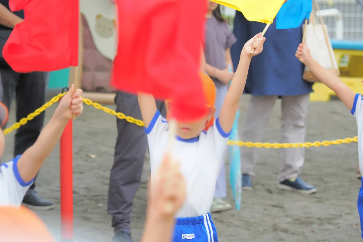 OM-1で撮影された、運動会で旗を振る子供と、手前のぼやけた旗が写る写真