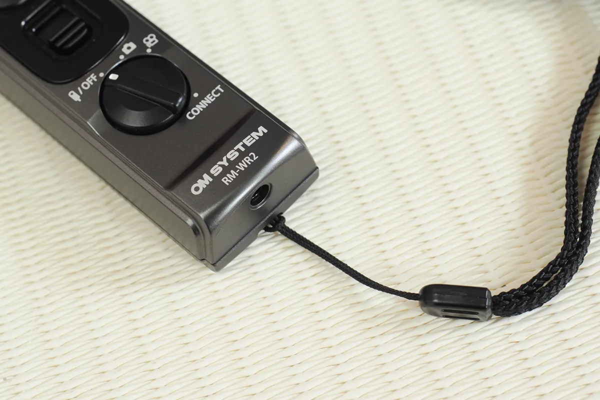 OM SYSTEM RM-WR2ワイヤレスリモコンに装着されたストラップと物理電源ダイヤル
