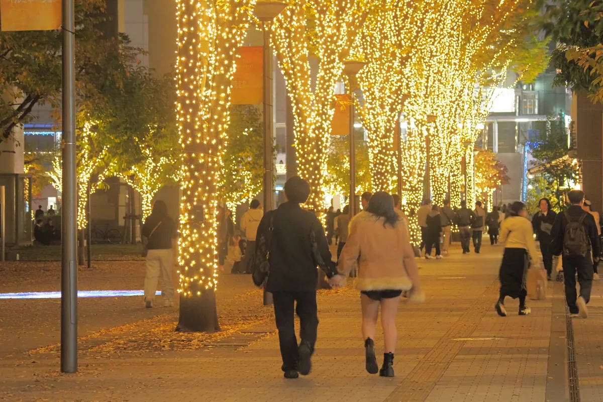 夜の立川イルミネーション、黄金色のライトで飾られたケヤキ並木を歩く人々。