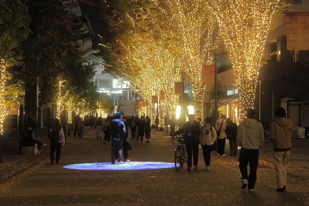 イルミネーションで飾られた通りに、円形のプロジェクションマッピングが投影され、人々が歩いている様子。