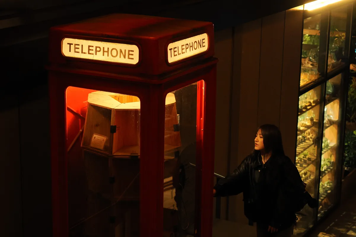 立川グリーンスプリングスの夜景。赤い電話ボックスが鮮やかに光り、その前に一人の女性が佇んでいる。背景にはぼやけたイルミネーションの光が広がる。