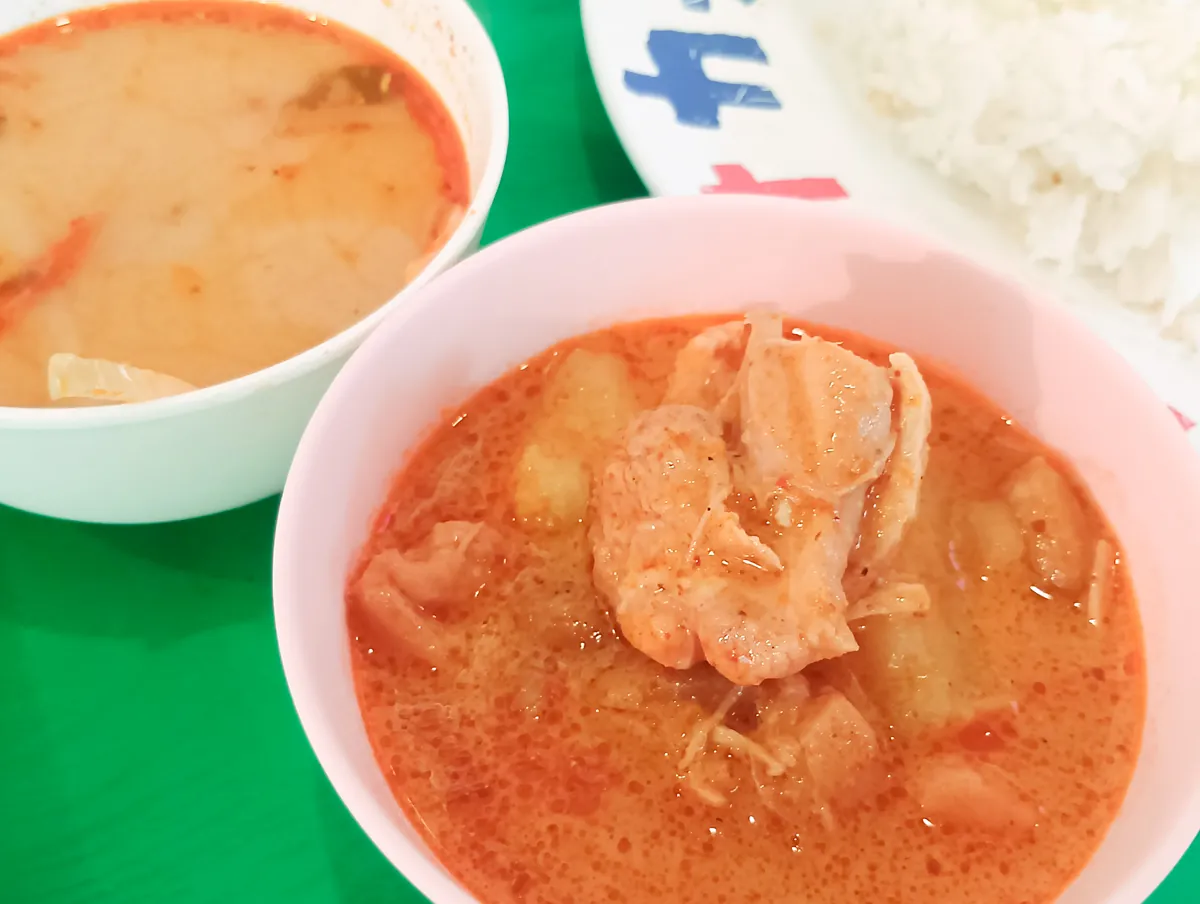 小さな白い器に入った赤いカレー。鶏肉とジャガイモのような具材が見える。