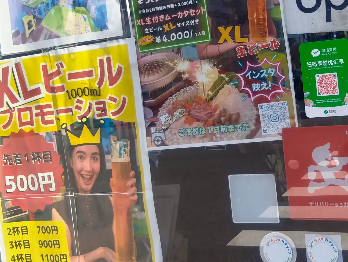 XLビールプロモーションの看板。女性が大きなビールジョッキを持ち、笑顔で写っており、先着1杯500円、2杯目700円、3杯目900円、4杯目1100円と書かれている。