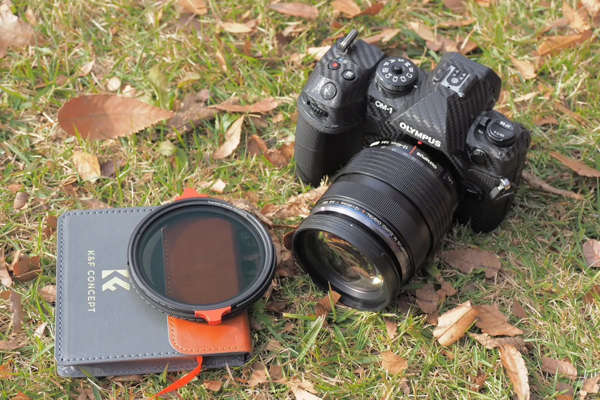 K&amp;F CONCEPT 2-in-1フィルターとOM-1カメラ、フィルターケース。カメラの隣にあるフィルターが強調され、その横には専用のフィルターケースが置かれている。