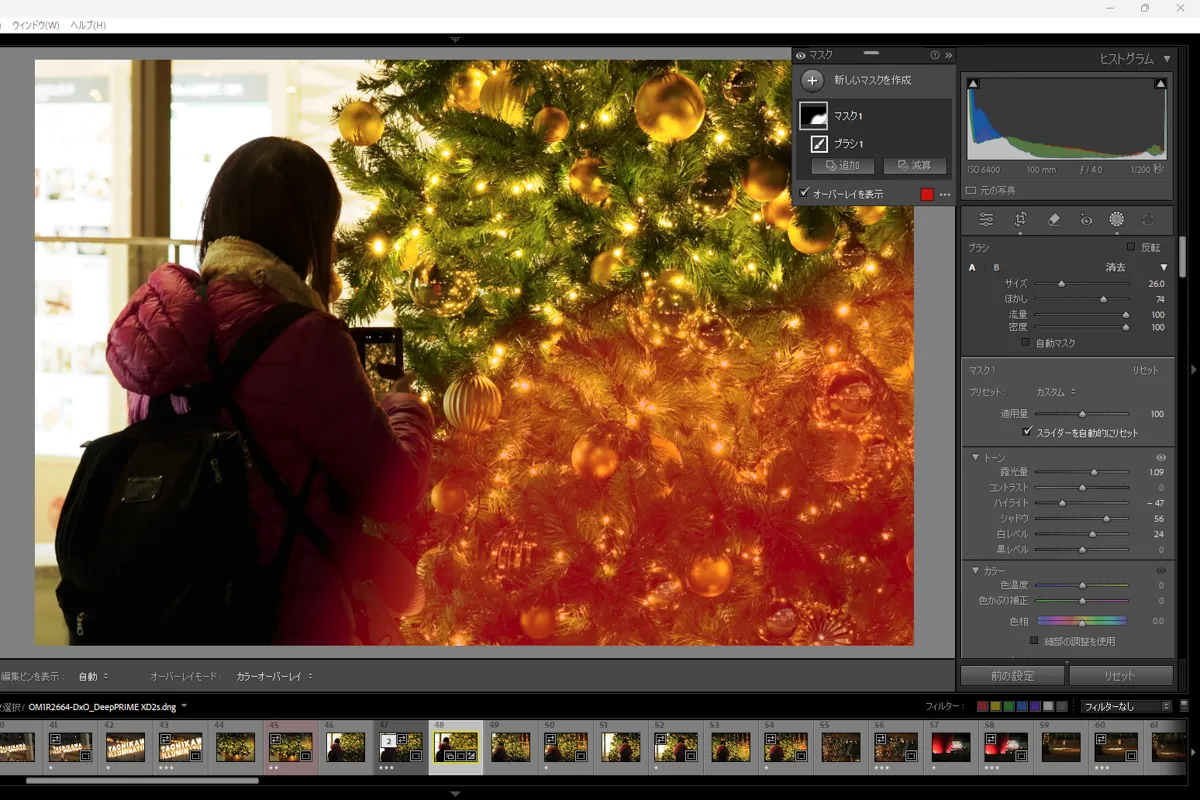 Lightroom Classicの編集画面。大きなクリスマスツリーの前で撮影する人物の背景に、ブラシツールでマスクを作成している様子