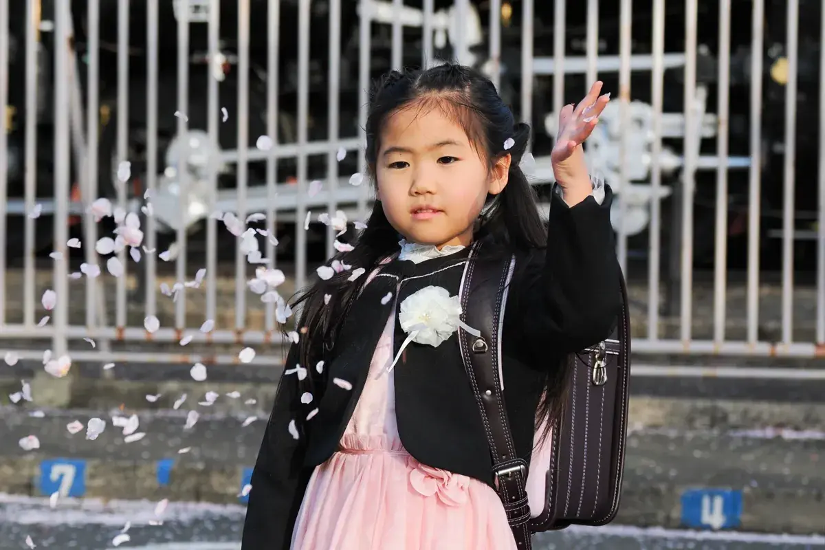 桜の花びらを手で散らす女の子。花びらが宙に舞っている瞬間。ランドセル姿。
