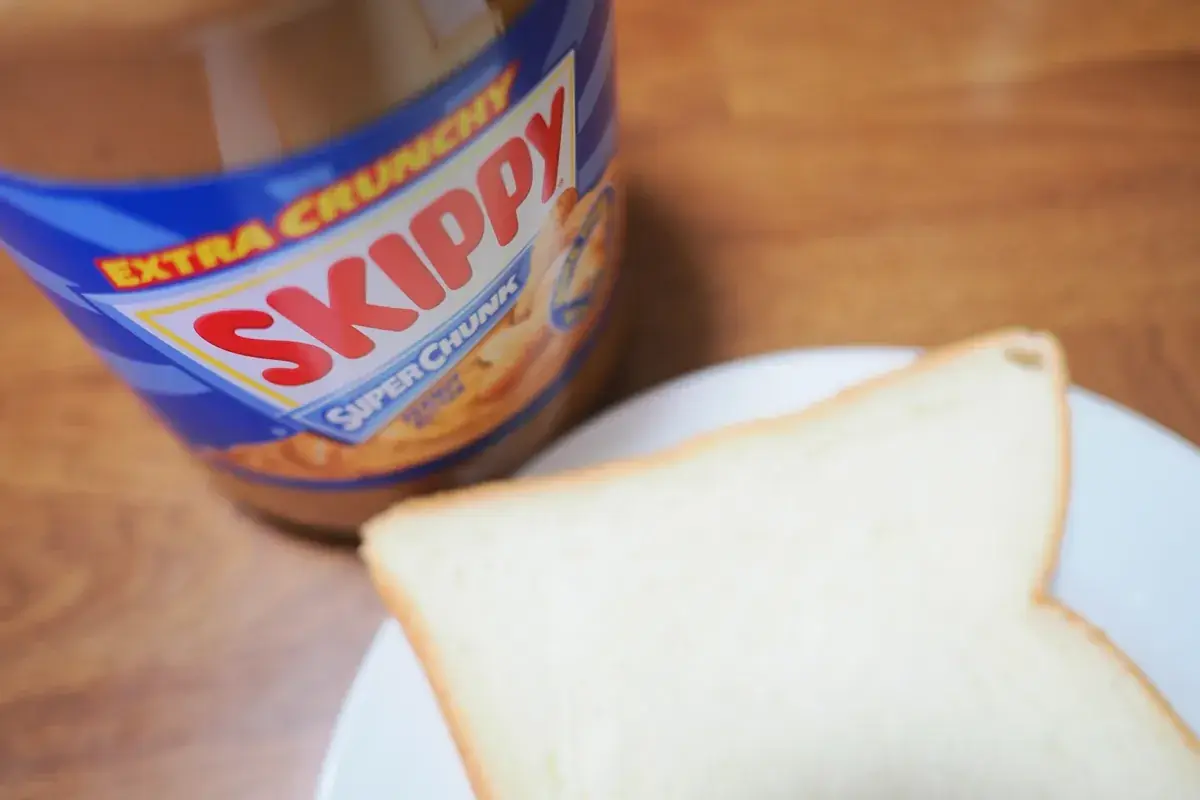 SKIPPYピーナッツバターの青いラベルと、手前に置かれた食パン。背景は木目調のテーブルで温かみのある雰囲気