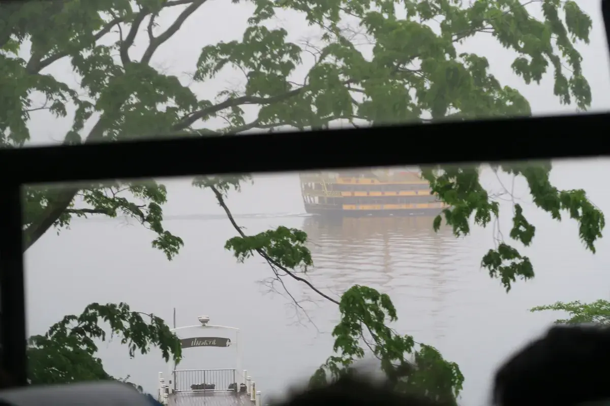 バスの窓越しに撮影した芦ノ湖の遊覧船。窓ガラスの指紋と雨粒が写り込み、船は霧に霞む。