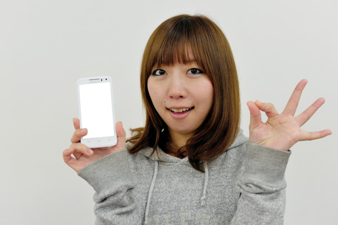 スマホを握ってOKサインを出している女の写真