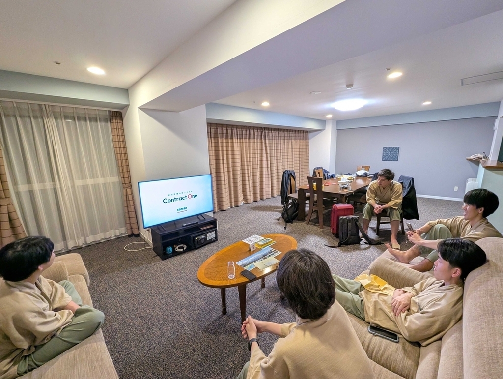 部屋に集まってテレビを囲み、ContractOneのCMを鑑賞している
