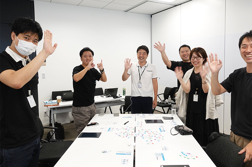 「プライドパレードに参加する」という思い出カードを引き、カードに書かれた指示通り笑顔で手を振る参加者たち。