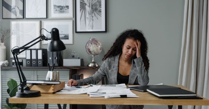 オフィスのデスクで、片手を頭に添えうつむく女性