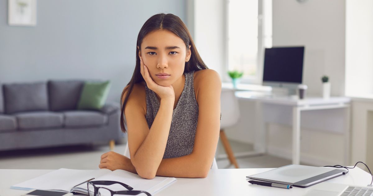 デスクにて、やる気がなさそうな表情で頬杖をつく女性