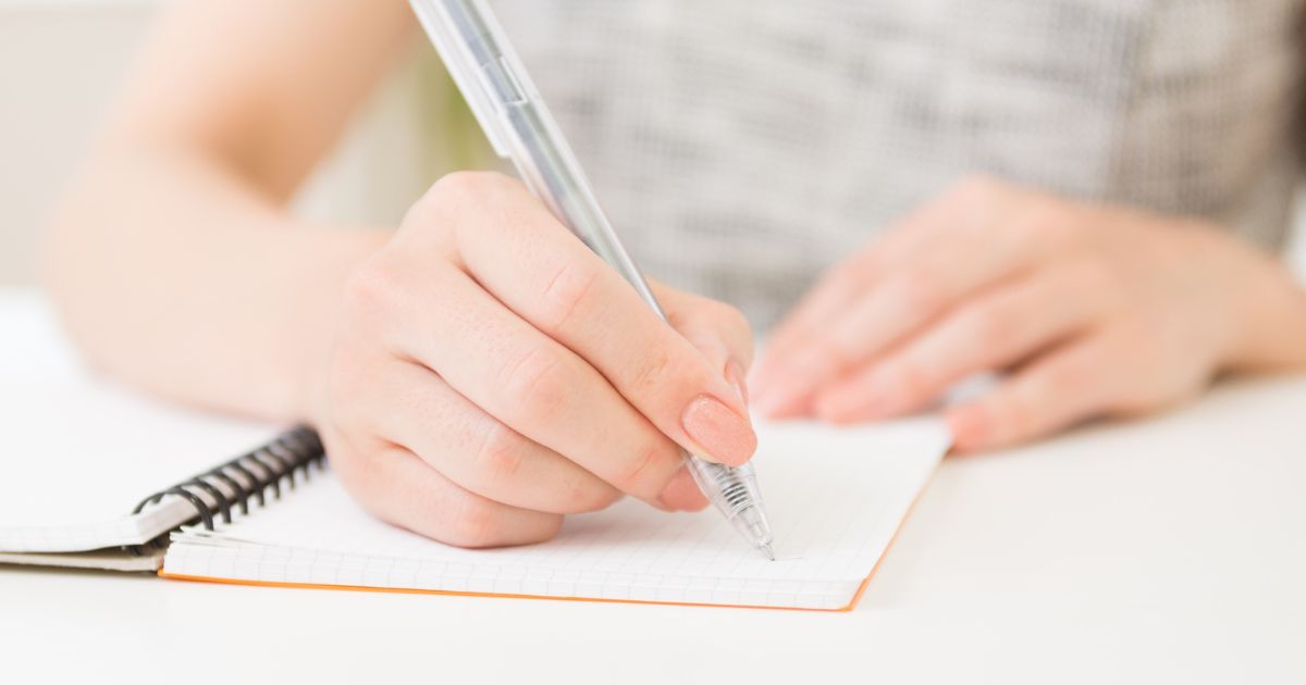 ペンを持ちメモを書いている手元のアップ