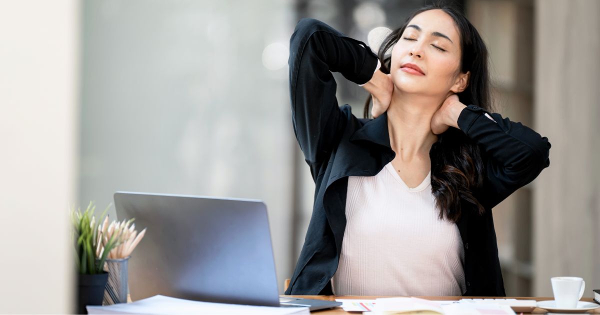 デスクに座り両手を首の後ろに組みながら目を瞑る女性ビジネスパーソン