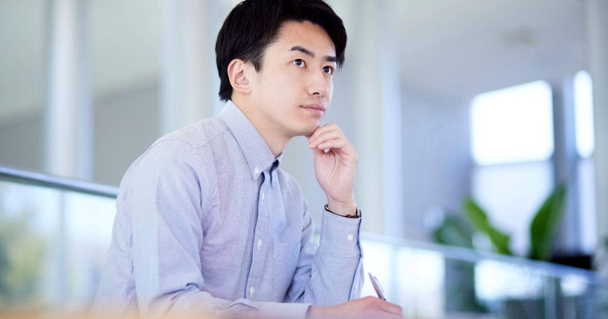 ノートとペンを手に考えごとをするビジネスパーソン。新しいアイデアを思案している様子。