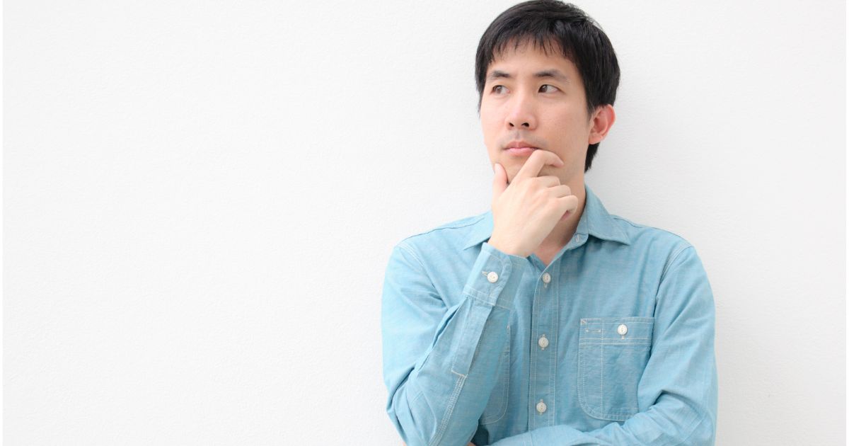 顎に手を当て、真剣な表情で考え込む男性。決断を前に迷いながらも冷静に思案している様子