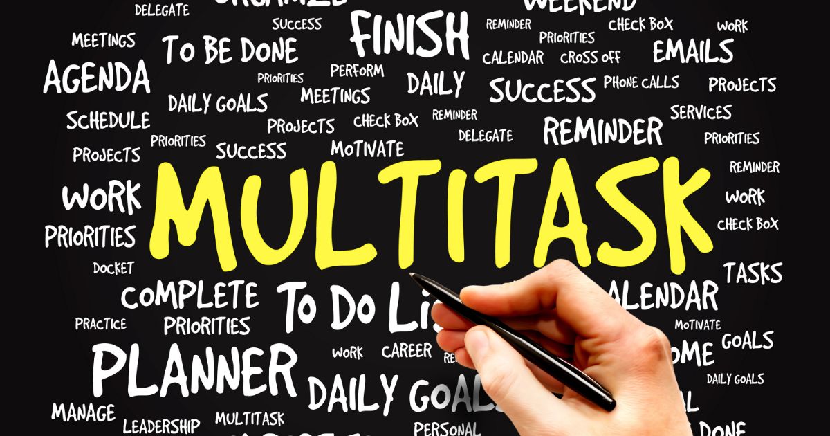 「MULTITASK」と大きく書かれた黒板の前で、ペンを持つ手
