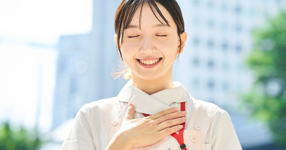 屋外で目を閉じ、胸に手を当てて微笑む女性。