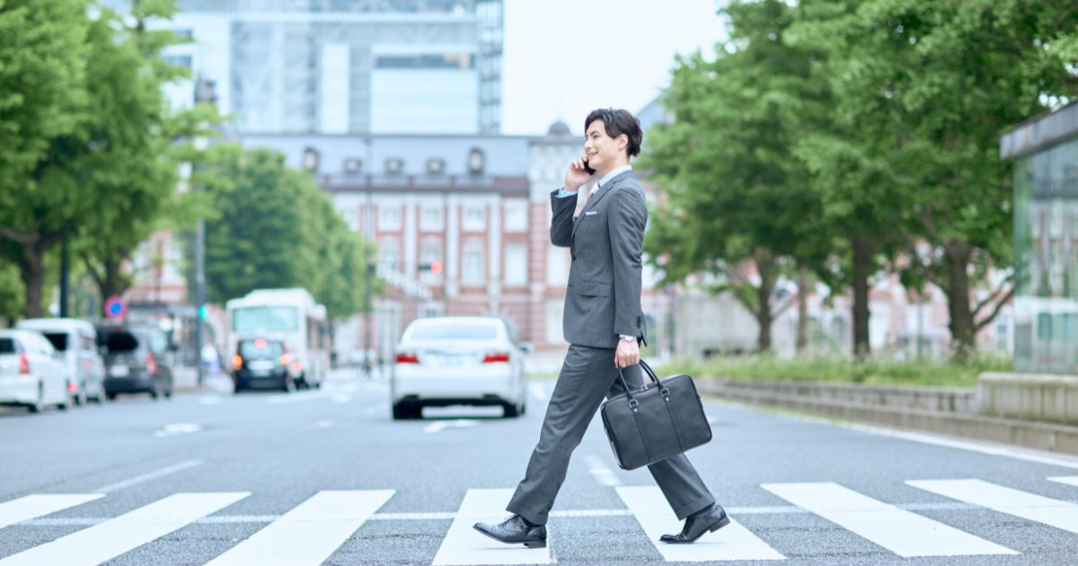 スーツ姿の男性が、横断歩道を渡りながらスマートフォンで通話している