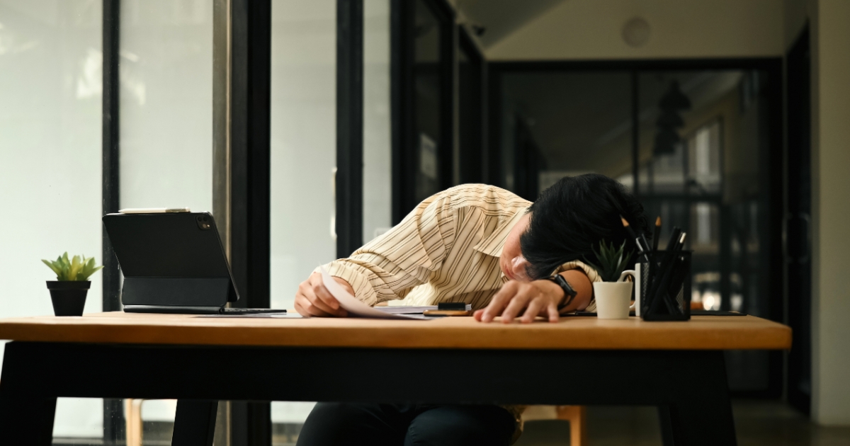 仕事の疲れからオフィスのデスクに突っ伏して眠るビジネスパーソン
