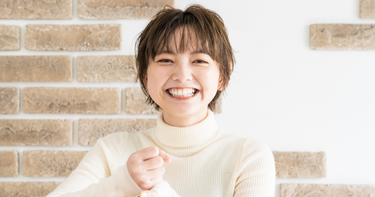 レンガ調の壁の前で笑顔のショートヘアの女性