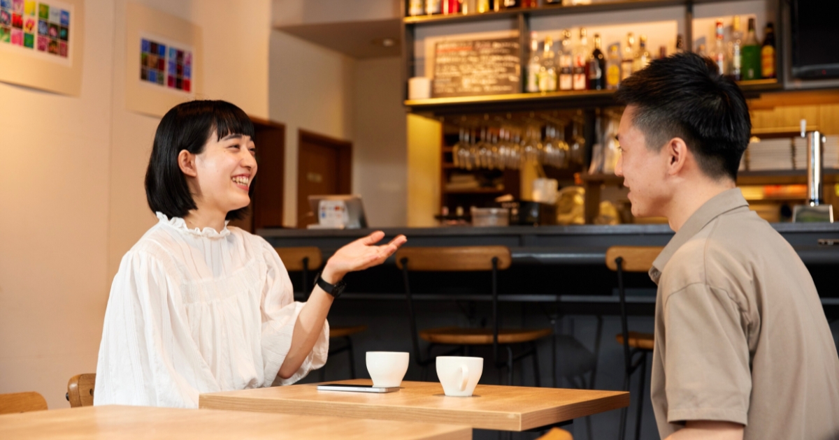 カフェで向かい合って会話する男女。身振り手振りを交えてリラックスした雰囲気で話している