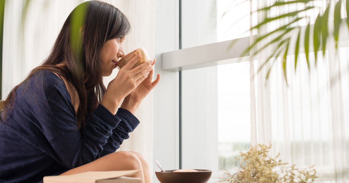 窓の外を見ながらコーヒーを飲んでいる女性