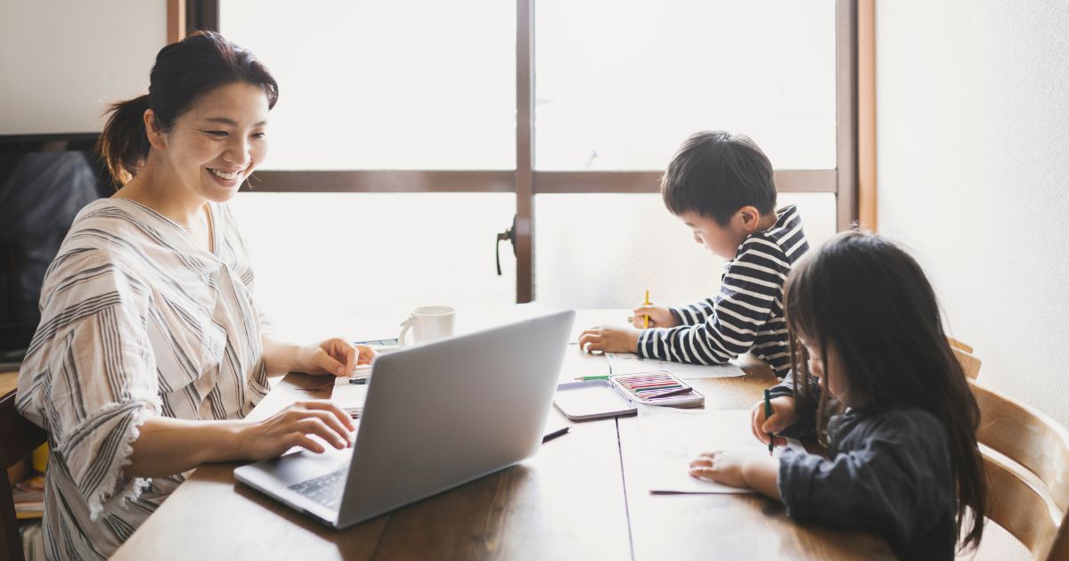 仕事をしている女性の向かいに座って勉強している子供たち