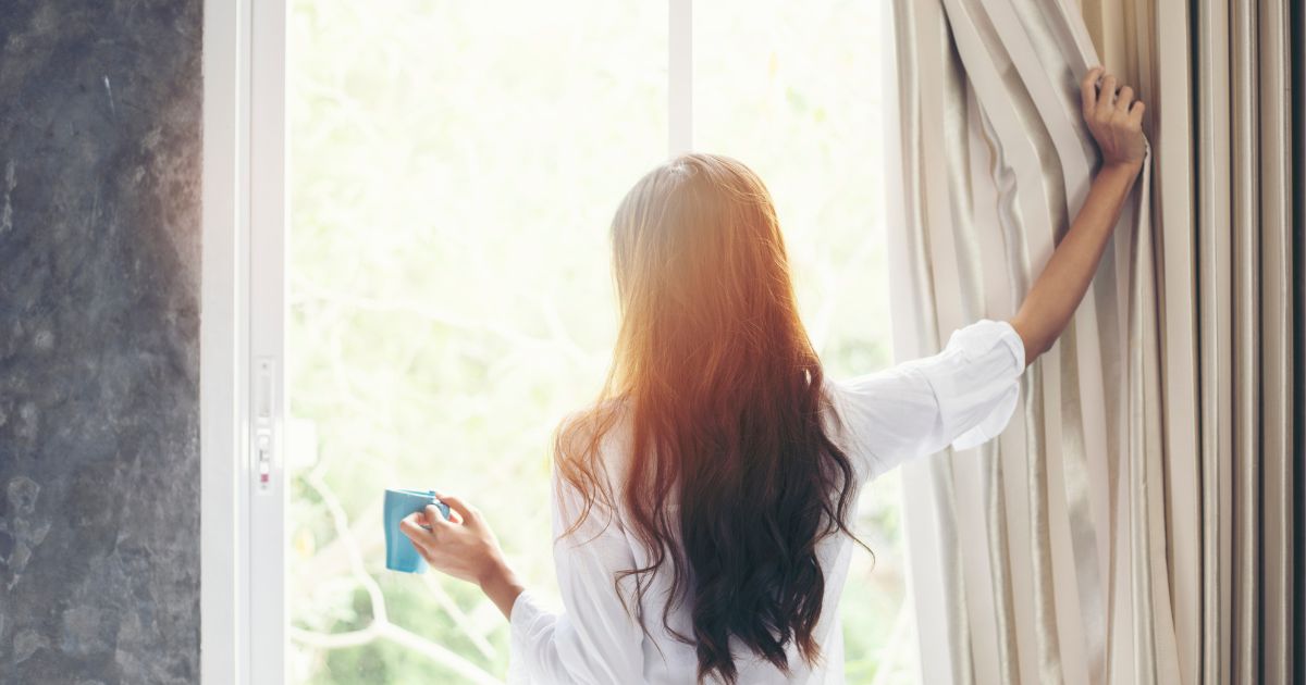 目覚めてカーテンを開ける女性